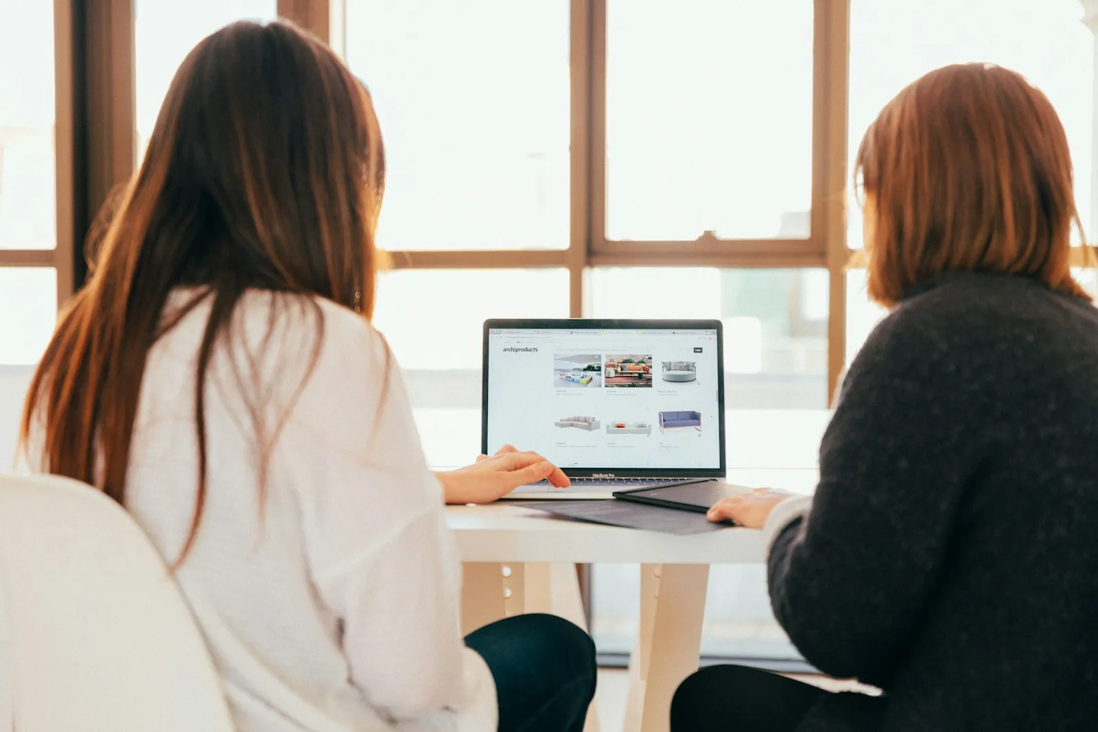 Duas pessoas trabalhando em laptops em uma mesa perto de uma janela