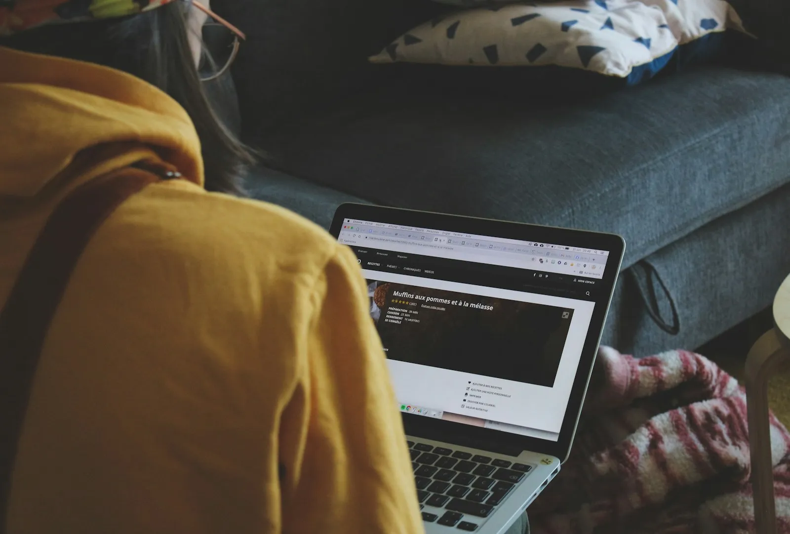 Person in a yellow jacket typing on a laptop on a couch